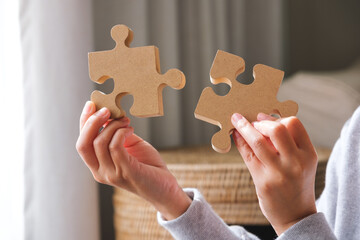 Closeup image of hands holding and putting a piece of wooden jigsaw puzzle together