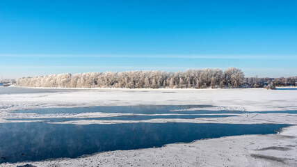 Atmospheric view of a snow-covered forest on the riverbank of a frozen river.