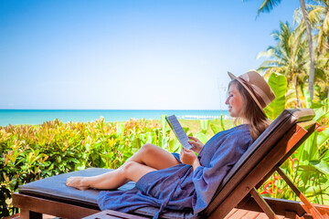 Fototapeta premium Happy young woman relaxing on wooden deck chair at luxury villa