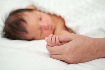 Obraz na płótnie Canvas mother holding hand of sleeping newborn baby on bed
