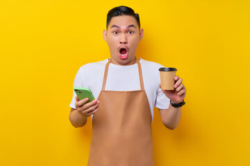 Shocked young Asian man barista barman employee wearing brown apron work in coffee shop holding...