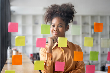 Fototapeta Young smiley attractive, businesswoman using sticky notes in glass wall to writing strategy business plan to development grow to success obraz