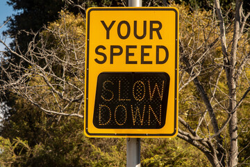 Yellow digital sign measuring traffic speed. The sign says Your Speed  and shows Slow Down in...