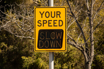 Yellow digital sign measuring traffic speed. The sign says Your Speed  and shows Slow Down in...