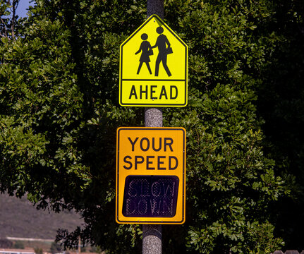 Yellow digital sign measuring traffic speed. with a school zone sign. The sign says Your Speed  and shows Slow Down in digital letters