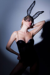 Beautiful sexy woman with large breasts wearing carnival black mask of Easter bunny rabbit. Blonde girl posing near gray wall in studio. Sexy bunny woman.