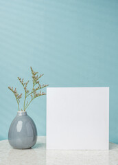 blank poster paper card with flower vase decor on stone table wtih blue background