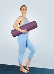A slender girl in a blue tracksuit holds a yoga mat. The instructor goes to class.
