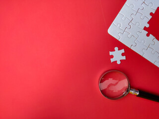Magnifying glass searching missing puzzle on red background