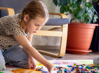 Build a blocks house out of bricks. Little blonde girl plays with colorful toy blocks at home,...