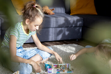 Two little sister girls play with multi-colored toy blocks at home in the living room. Educational...