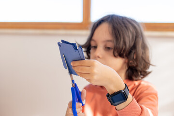 The child cuts colored paper with scissors at the table. the boy cuts a snowflake out of blue paper with scissors.