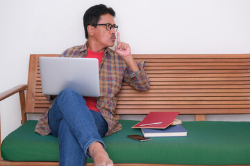 A man sitting on green sofa, working his office business on his laptop from home