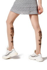 Cropped shot of a slim lady wearing a skirt, sneakers and beige tights with a color print imitating tattoo at the back. The tempting woman in tattoo-effect tights is posing on a white background.