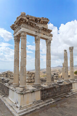 Fototapeta premium The ruined Temple of Trajan in Pergamon Ancient City. Corinthian order stone-cut relief on the frieze. Dramatic sky at background. History, art or architecture concept. Bergama, Turkey