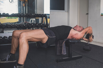 A rugged and old German man does dumbbell pullovers while lying perpendicular to the bench....