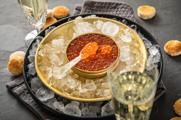 Orange Keta Lachs Kaviar in Dose auf Eis in Glas Schale mit Perlmutt Löffel, Sekt Champagner und Toast Brot auf dunkel Serviette und schwarz Schiefer