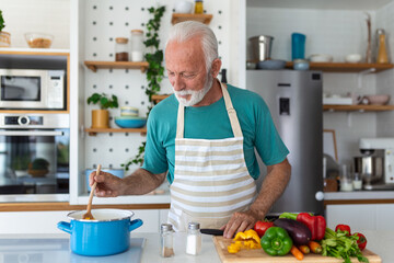 Happy senior man having fun cooking at home - Elderly person preparing health lunch in modern kitchen - Retired lifestyle time and food nutrition concept