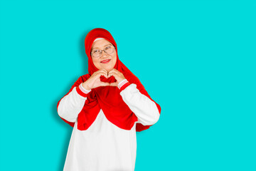 Senior muslim woman with glasses smiling in love doing heart symbol shape with hands