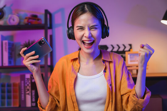 Excited Young Asian Woman Playing An Online Game On A Smartphone With Fists Clenched Celebrating Victory Expressing Success.