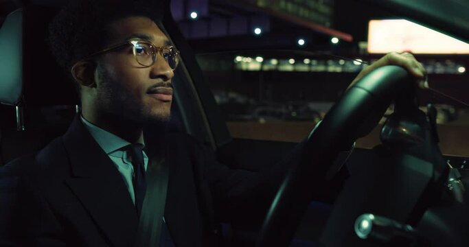 Portrait of A Handsome Black Man in a Suit Driving a Fancy Car at Night and Focused on the Road. Successful African American Businessman Driving Back Safely from Work, Following Traffic Signals