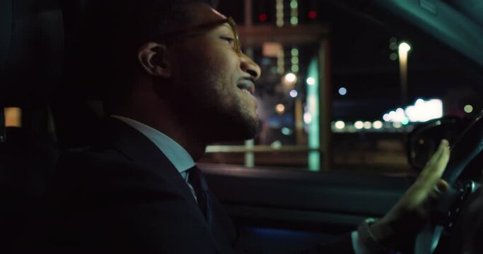 Portrait of A Handsome Black Man in a Suit Dancing in his Car at Night. Successful African American Businessman Enjoying his Time Listening to Radio and Music While Waiting for Traffic 