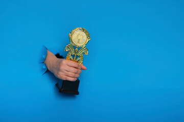 image of trophy in hand, concept for winning or success. Golden trophy on blue background, top view...
