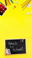 black chalk board with handwritten Back to school supplies chalk, felt-tip pens, paints, pen, paper clips, band on yellow background top view