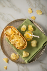 Gelber Saiblings Kaviar mit Perlmutt Löffel zu Kartoffelchips Chips in Korb als Gourmet Snack auf Serviette grün, Silber Teller und Marmor hell