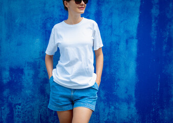 Female model wearing white blank t-shirt on the background of an blue wall.