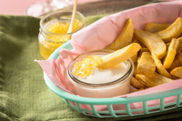 Gelber Saiblings Kaviar mit Perlmutt Löffel zu Pommes, Saure Sahne und Champagner Sekt in Korb rosa auf Serviette grün und Hintergrund Pastell Pink