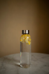 minimalistic refillable water bottle with lemon closeup. closed plastic bottle of lemon water on marble table macro