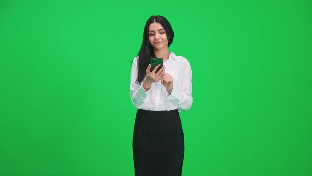 Slow motion, elegant woman in a suit standing on chromakey background, using smartphone and looks at the screen, surfing the internet, green background, chromakey template.