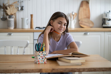 Portrait of happy schoolgirl learning at home with textbook. Smiling little kid girl sits at desk...