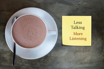 Chocolate cup on table with note reminder LESS TALKING MORE LISTENING, to speak less and listen...