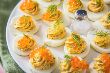 Gefüllte teuflische russische Eier mit Dill und orange Keta Lachs und gelb Saibling Kaviar auf Eierteller, Serviette grün, Silber Teller und Pastell Pink Rosa Hintergrund 