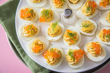 Gefüllte teuflische russische Eier mit Dill und orange Keta Lachs und gelb Saibling Kaviar auf Eierteller, Serviette grün, Silber Teller und Pastell Pink Rosa Hintergrund 