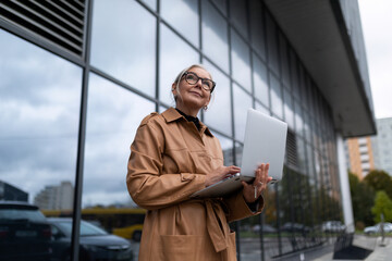 Business woman in a leather coat with a laptop in her hands against the backdrop of a glass facade of the office