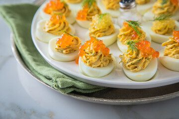 Gefüllte teuflische russische Eier mit Dill und orange Keta Lachs und gelb Saibling Kaviar auf Eierteller, Serviette grün, Silber Teller und Marmor Hintergrund hell