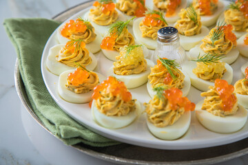 Gefüllte teuflische russische Eier mit Dill und orange Keta Lachs und gelb Saibling Kaviar auf Eierteller, Serviette grün, Silber Teller und Marmor Hintergrund hell