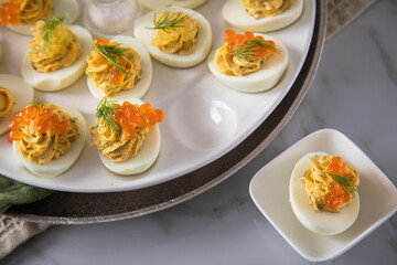 Gefüllte teuflische russische Eier mit Dill und orange Keta Lachs und gelb Saibling Kaviar auf Eierteller, Serviette grün, Silber Teller und Marmor Hintergrund hell