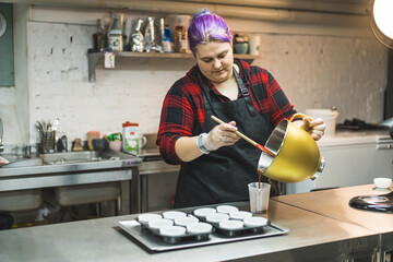 medium shot of a female chef with purple hair putting dough from a bowl into a mug to add to...