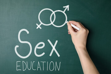 Sex education. Woman drawing male gender sign on green chalkboard, closeup