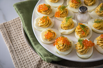 Gefüllte teuflische russische Eier mit Dill und orange Keta Lachs und gelb Saibling Kaviar auf Eierteller, Serviette grün, Silber Teller und Marmor Hintergrund hell