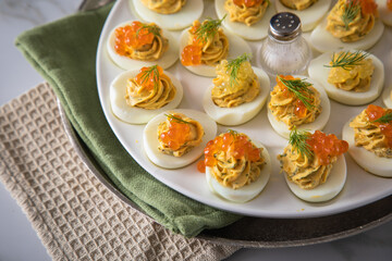 Gefüllte teuflische russische Eier mit Dill und orange Keta Lachs und gelb Saibling Kaviar auf Eierteller, Serviette grün, Silber Teller und Marmor Hintergrund hell