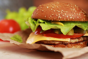 Cheeseburger on a paper napkin close-up. Burger with chicken cutlet, melted cheese, salad and vegetables. Fast food