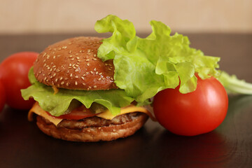 Cheeseburger close up. Homemade burger and tomatoes nearby. Fast food