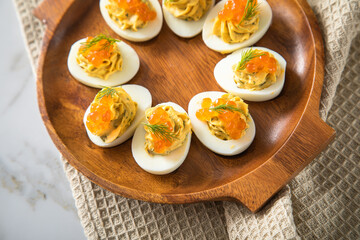 Gefüllte teuflische russische Eier mit Dill und orange Keta Lachs Kaviar auf Holz Eierteller, Serviette und Marmor Hintergrund hell