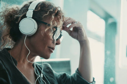 Side portrait of a woman with headphones listening music or podcast alone. Thoughtful female people at work. Indoor leisure activity at home. Attractive lady touch her front worried. People problems