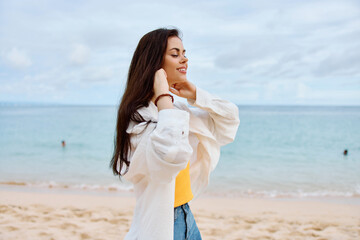 Fototapeta na wymiar Happy woman smile with teeth with long hair brunette walks along the beach in a yellow t-shirt denim shorts and a white shirt near the sea summer journey and feeling of freedom, balance